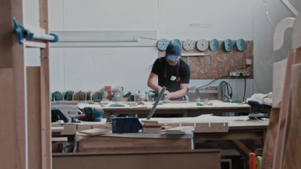 Hombre en un taller de carpintería moliendo una pieza de madera — Vídeos de Stock