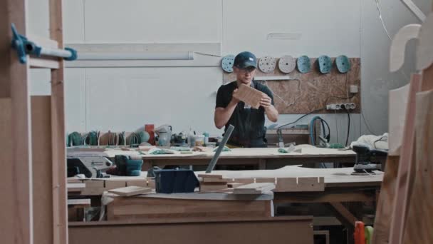 Ο άνθρωπος σε ένα εργαστήριο ξυλουργικής κοιτάζοντας το αλεσμένο ξύλινο κομμάτι — Αρχείο Βίντεο