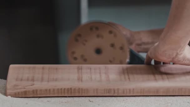 Man werker maakt de zijkant van een houten detail zachter met behulp van een slijpmachine — Stockvideo