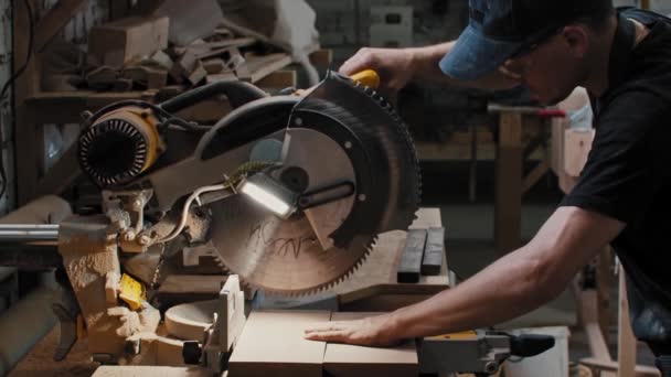 Timmerwerk - arbeider zet een grote cirkelzaag over het houten detail en brengt het naar de hoek van het detail — Stockvideo
