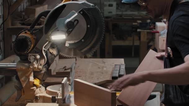 Timmerwerk - arbeider legt twee houten stukken onder een grote cirkelzaag — Stockvideo