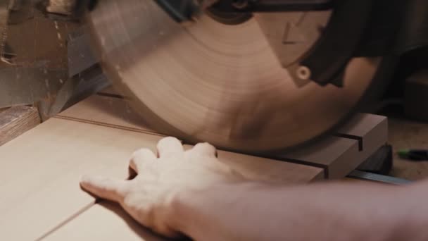 Человек в столярной мастерской делает зарубки на деревянных деталях с помощью большой циркулярной пилы — стоковое видео
