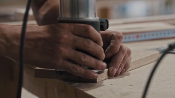 Homem em uma oficina de carpintaria trabalhando com uma peça de madeira usando um instrumento de corte — Vídeo de Stock