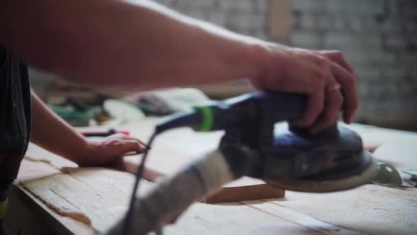 Timmerwerk in werkplaats - arbeider die het oppervlak van een houten detail slijpt — Stockvideo