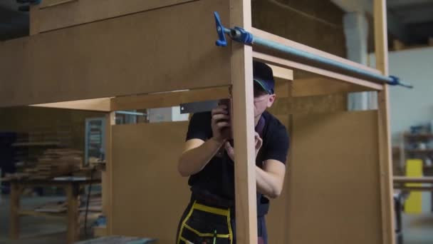Trabajos de carpintería en taller - trabajador de pie en la construcción de madera inacabada y midiendo el espacio para los detalles — Vídeos de Stock