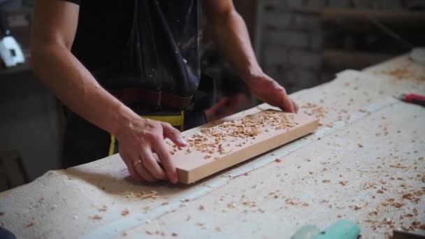 Travaux de menuiserie en atelier - l'ouvrier amène la planche de bois à la table et secoue les copeaux — Video