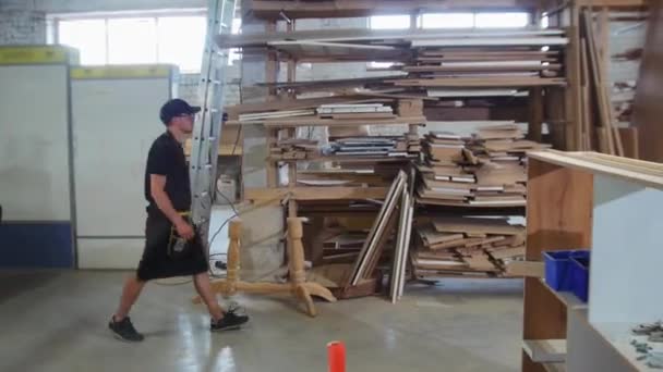 Warsztat stolarski - pracownik spaceruje po półkach i bierze trójkątną deskę — Wideo stockowe