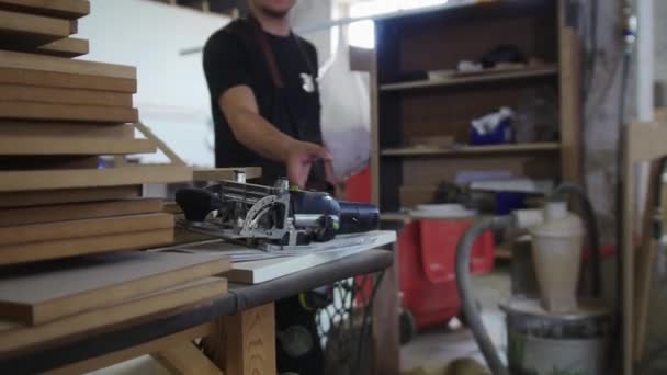 Taller de carpintería - un trabajador camina por el estudio y toma la amoladora - mirando a la cámara — Vídeos de Stock