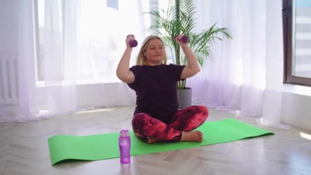 Fitness školení -blondýny nadváha žena dělá fitness cvičení s činkami pak pije vodu z láhve — Stock video