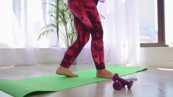 Фитнес-тренировка - блондинка с избыточным весом садится на коврик для йоги и ставит беспроводные наушники — стоковое видео