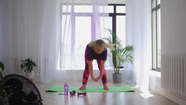 Fitnesstraining - blonde vrouw met overgewicht die fitnessoefeningen doet - haar lichaam opwarmen met bukken op de grond — Stockvideo