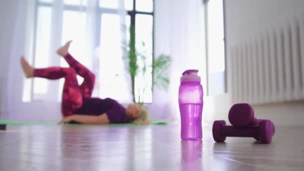 Fitness training - vrouw met overgewicht die op haar rug ligt en traint voor haar benen - fles en kleine halters op de voorgrond — Stockvideo