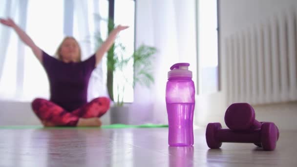 Allenamento fitness - donna sovrappeso che medita sul tappetino yoga - una bottiglia d'acqua e piccoli manubri in primo piano — Video Stock