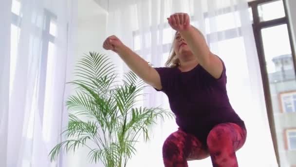 Fitness träning - överviktig kvinna knäböjer på yogamattan i vitt rum — Stockvideo