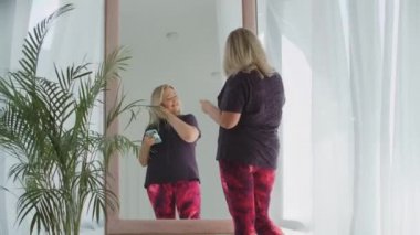 Sarışın, kendine güvenen şişman kadın kulaklığına kablosuz kulaklık takar ve aynanın önünde dans etmeye başlar.