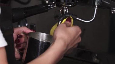 Dişi barista kapuçino için süt köpürür ve buhar musluğunu bir bezle siler.