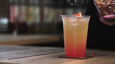Barmen alkollü bir içeceğin üstüne kurumuş portakal parçaları koyar.