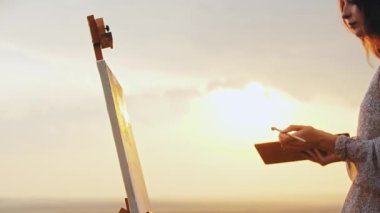 Gün batımında resim çizen genç bir kadın.