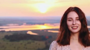 Çilli, güzel yüzlü, günbatımı sahasında zıplayan ve kameraya gülümseyen genç bir kızıl kadın.