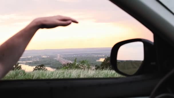 Mężczyzna wyciąga rękę przez okno samochodu i bawi się strumieniem powietrza - przechodząc przez pola i jeziora — Wideo stockowe