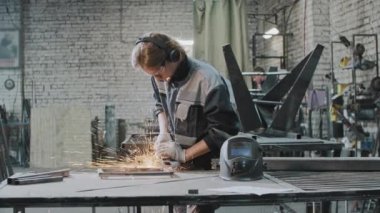 Koruyucu gözlüklü genç adam imalat fabrikasında çalışıyor. Metal inşaatı çim biçme makinesiyle öğütüyor.