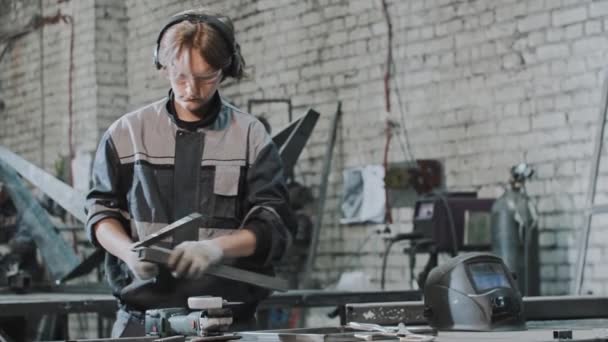 Fabrikada çalışan koruyucu gözlüklü genç adam metal işlerinde bir çentik atıyor. — Stok video