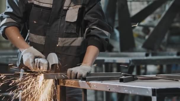 Młody człowiek w okularach ochronnych w zakładzie - cięcie konstrukcji metalowej szlifierką kątową — Wideo stockowe