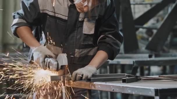 Młody człowiek pracujący w zakładzie - cięcie konstrukcji metalowej szlifierką kątową — Wideo stockowe