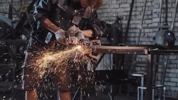 Молодой человек, работающий на заводе - отрезает кусок металла с помощью угловой мельницы — стоковое видео