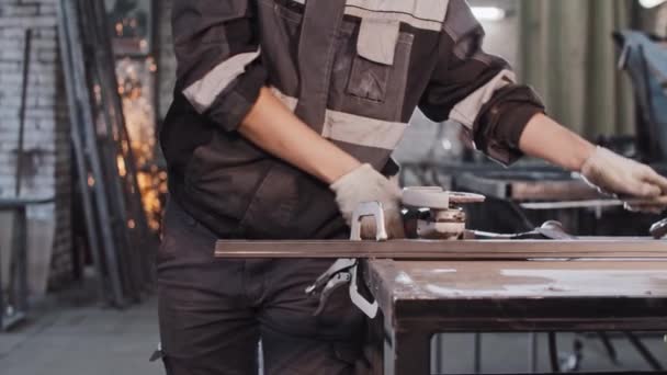 Młody człowiek z długimi włosami pracujący w zakładzie produkcyjnym - szlifowanie detali metalowych — Wideo stockowe