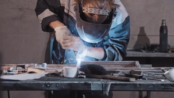 Młody pracownik w rękawiczkach ochronnych i hełmach spawalniczych części metalowych detali razem — Wideo stockowe
