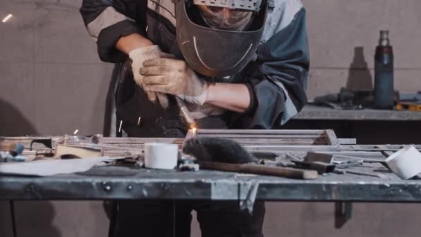 Młody pracownik w rękawiczkach ochronnych i hełmach spawalniczych części metalowych detali razem — Wideo stockowe