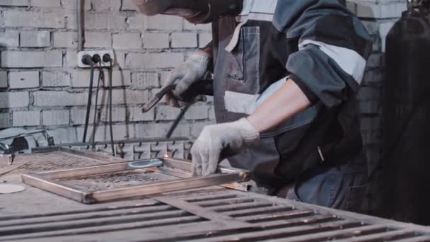 Junger Mann mit Schutzhelm schweißt Teile des Metallstücks am Tisch zusammen — Stockvideo