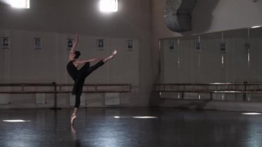 Siyah etekli profesyonel kadın balerin boş bir ayna stüdyosunda dans ediyor.