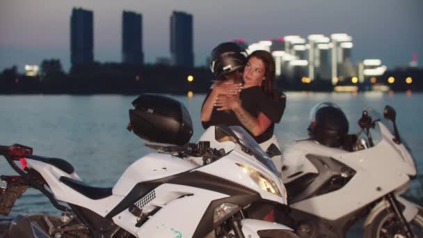 Duas amigas se encontrando perto da água da cidade noturna e se preparando para andar de moto — Vídeo de Stock