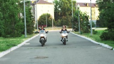 Akşamın erken saatlerinde kasksız iki kadın motosiklete biniyor.