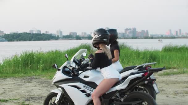 Zwei Freundinnen mit Helmen sitzen auf Motorrädern in der Nähe des Wassers in der Innenstadt und unterhalten sich — Stockvideo