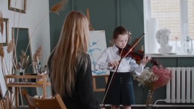 Sarışın kadın öğretmeniyle keman çalan bir kız.