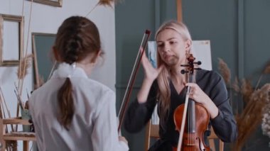 Genç bayan öğretmen küçük bir kızla keman dersi alıyor.