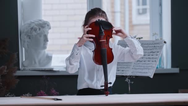 Маленькая девочка кладет скрипку под подбородок и смотрит в камеру — стоковое видео