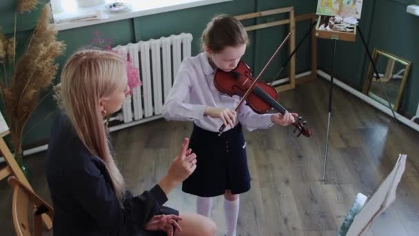 바이올린 교습 - 학급에서 바이올린을 연주하는 어린 소녀와 옆에 앉아 있는 금발의 여자 교사 — 비디오