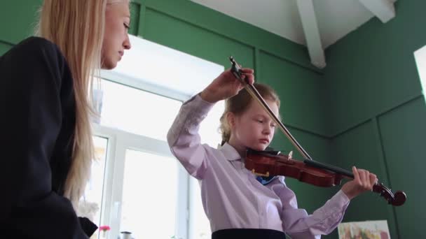 バイオリン教室-女の子のためにバイオリンを演奏します弓でクラスと彼女の先生座っています彼女の隣 — ストック動画
