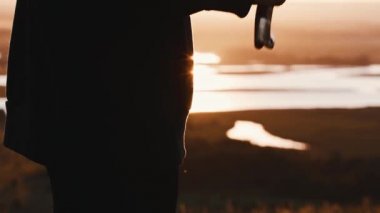 Gün batımında elinde kılıç tutan koyu renk elbiseli genç bir kadın.