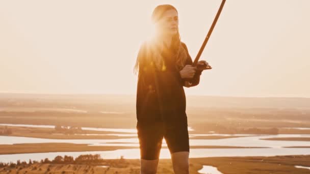 Gün batımında tepede kılıçlarla oynayan genç bir kadın. — Stok video