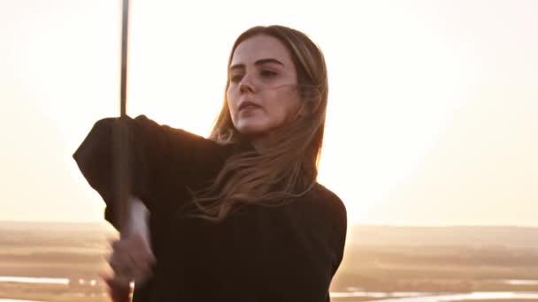 Молода красива жінка з довгим волоссям тренується з мечами на пагорбі під час заходу сонця — стокове відео