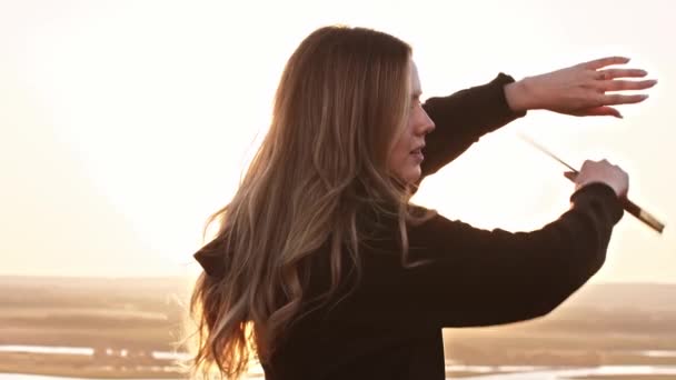 Giovane bella donna con i capelli lunghi formazione con una spada sulla collina mentre il tramonto — Video Stock