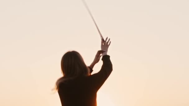 Young woman in black clothes swinging with a blade on bright orange sunset and throwing it up in the air — Stock Video