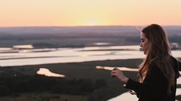 Jonge vrouw met lang haar zwaaien met een zwaard mes op heldere zonsondergang en kijkt in de camera — Stockvideo