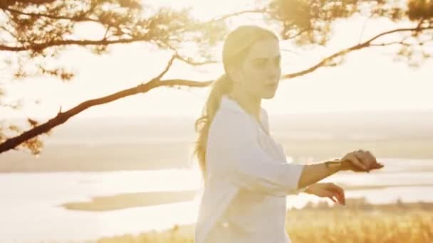 Wanita muda dalam kemeja putih melakukan permainan pedang di alam — Stok Video