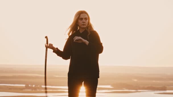 Jonge vrouw in zwart kleren spelen met een zwaard op zonsondergang — Stockvideo